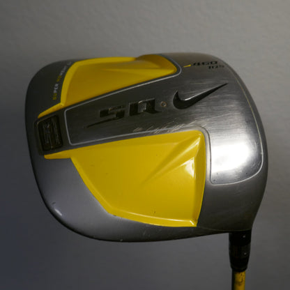 A Nike golf driver with a yellow and silver head, featuring the Nike swoosh and 'SQ' branding, shown against a plain gray wall.